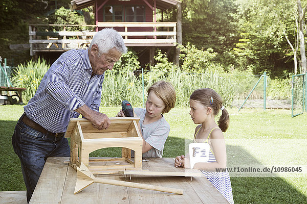 Großvater und Enkelkinder beim Bau eines Vogelhauses