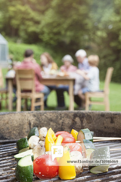 Gemüsespieße auf dem Grill mit Familie im Hintergrund