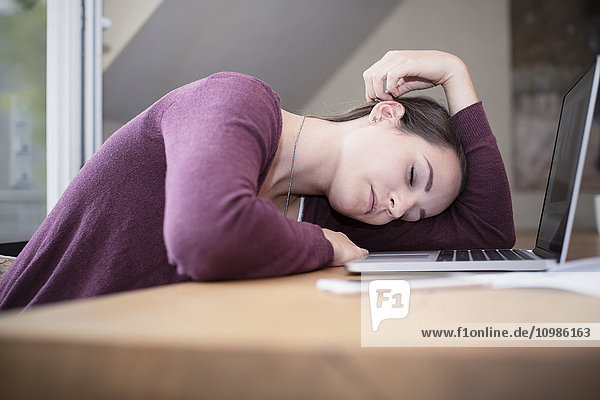 Müde junge Frau schläft am Schreibtisch