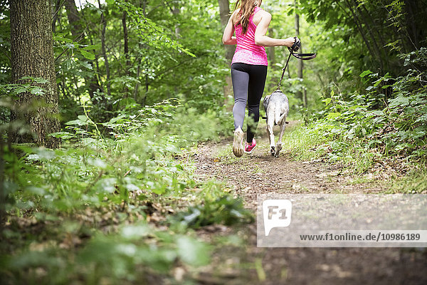Junge Frau beim Joggen mit Hund im Wald