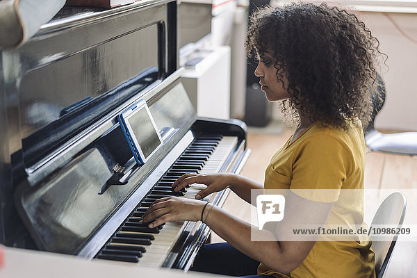 Young woman playing piano  reading notes from digital tablet