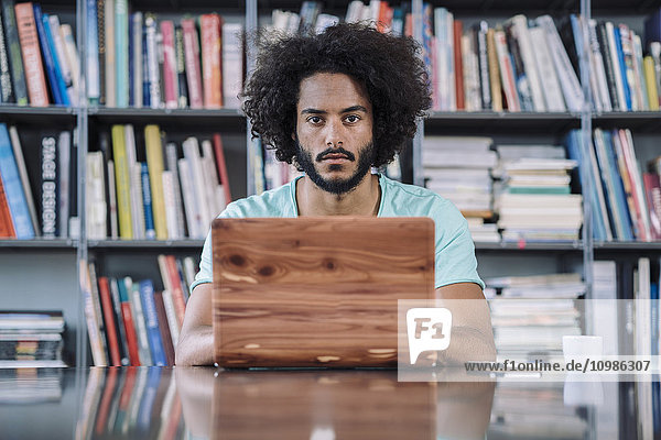 Junger Mann arbeitet in der Bibliothek  mit Holz-Laptop