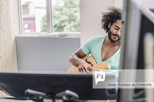 Junger Mann spielt Gitarre im Büro