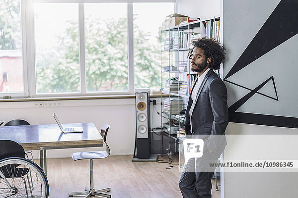 Young creative businessman standing in office  thinking with hands in pockets