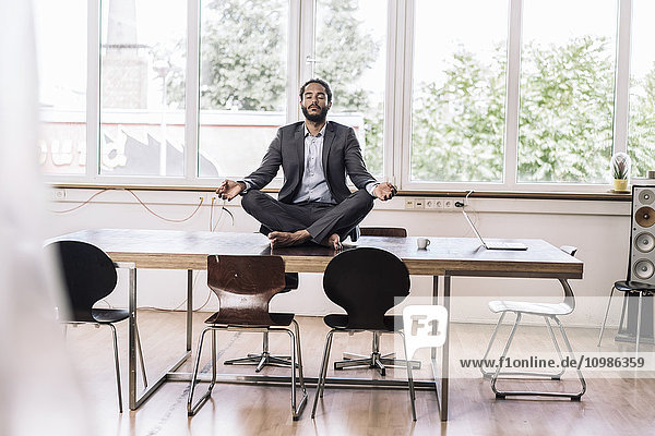 Young businessman sitting cross-legged on desk in office
