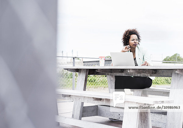 Nachdenkliche Geschäftsfrau  die draußen mit ihrem Laptop arbeitet.