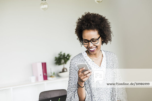 Lächelnde Geschäftsfrau im Büro mit Blick auf ihr Smartphone