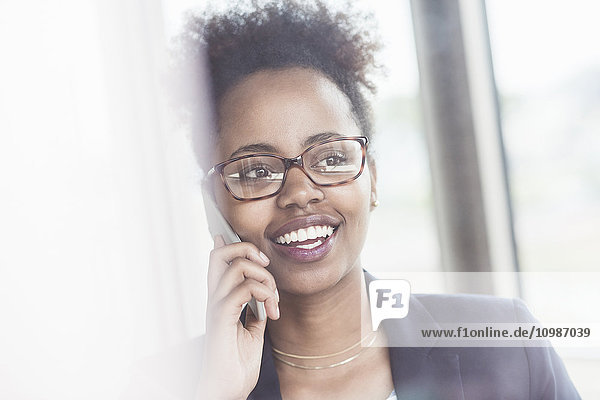 Porträt einer lächelnden Geschäftsfrau  die beim Telefonieren mit dem Smartphone durchs Fenster blickt