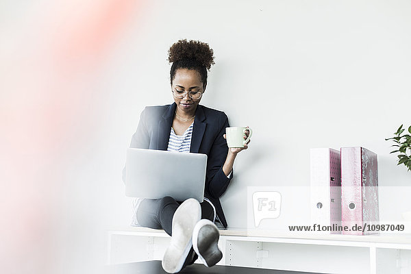 Lächelnde Geschäftsfrau mit Tasse Kaffee am Laptop