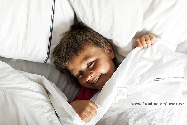 Smiling little boy lying in bed trying to sleep