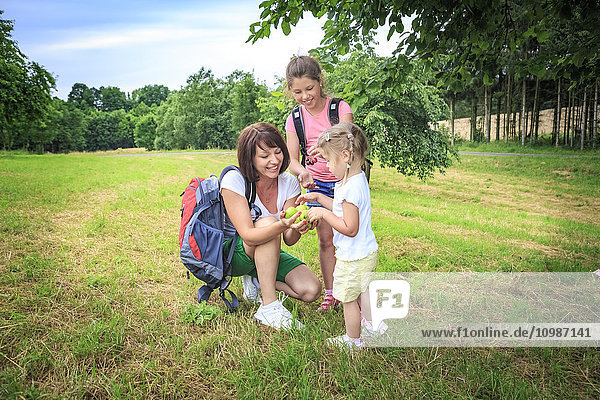 Mother giving apples  mother and daughters on meadow during hiking