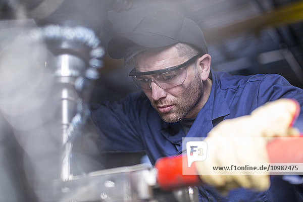 Mechaniker trägt Schutzbrille mit Bohrmaschine in der Werkstatt