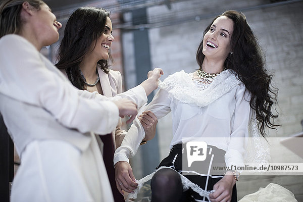 Fröhliche Schneiderinnen mit dem Kunden beim Anprobieren des Brautkleides