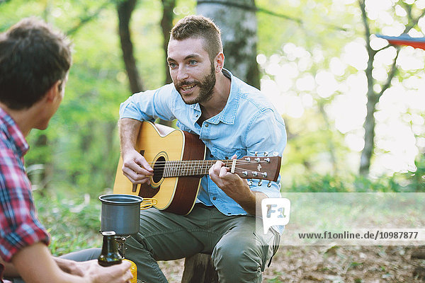 Friends playing guitar at a camp site