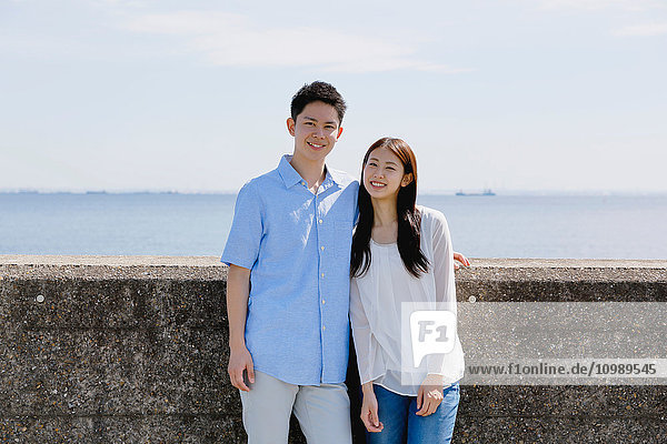 Young Japanese couple leaning on concrete wall by the sea