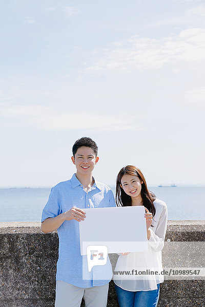 Young Japanese couple with whiteboard by the sea