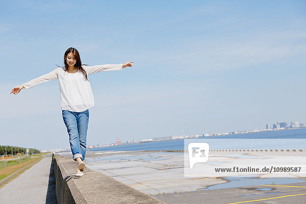 Young Japanese woman standing on concrete wall by the sea