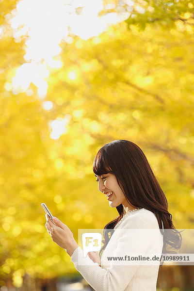 Junge Japanerin mit Smartphone in einem Stadtpark