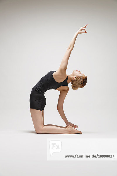 Attractive young Japanese woman wearing black pants and tank top practicing yoga on white background
