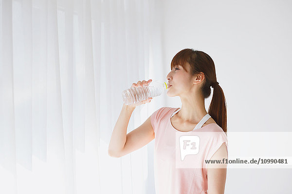 Young Japanese woman drinking water after practicing yoga
