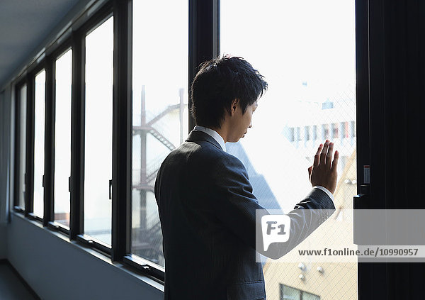 Japanese businessman looking out of the window in empty office
