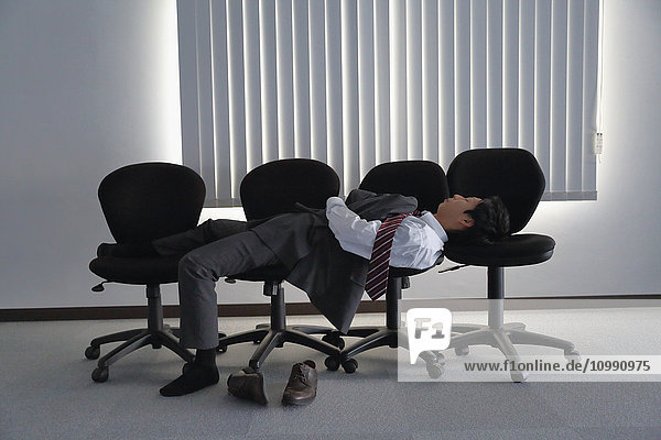 Japanischer Geschäftsmann schläft auf Stühlen
