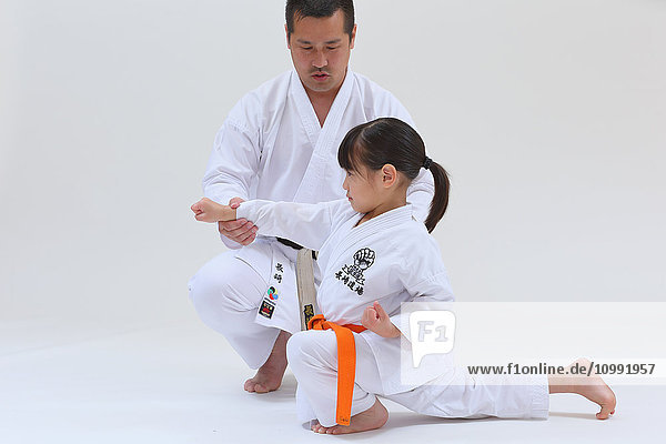 Japanisches Kind in Karate-Uniform Training mit Lehrer auf weißem Hintergrund