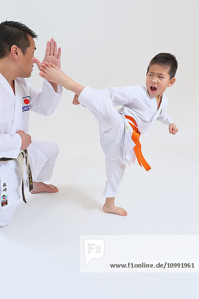 Japanese kid in karate uniform training with teacher on white background