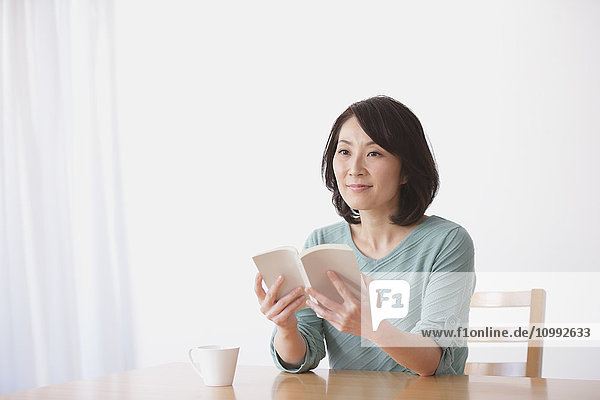 Ältere Japanerin mit Buch im Wohnzimmer