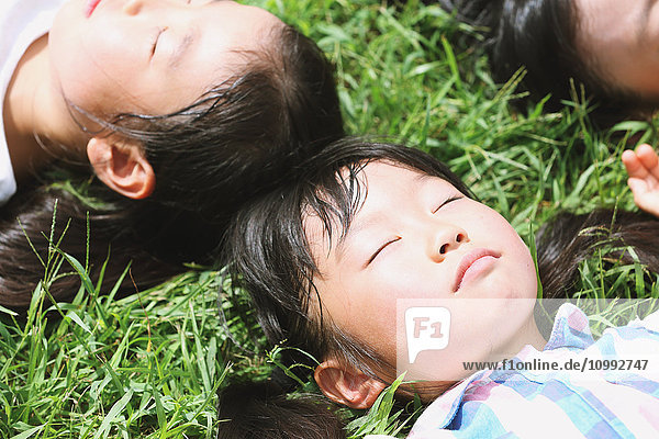 Japanische Kinder liegen im Gras in einem Stadtpark