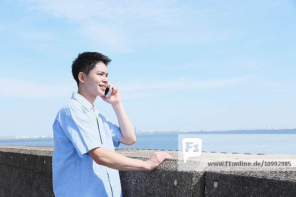 Young Japanese man on the phone by the sea