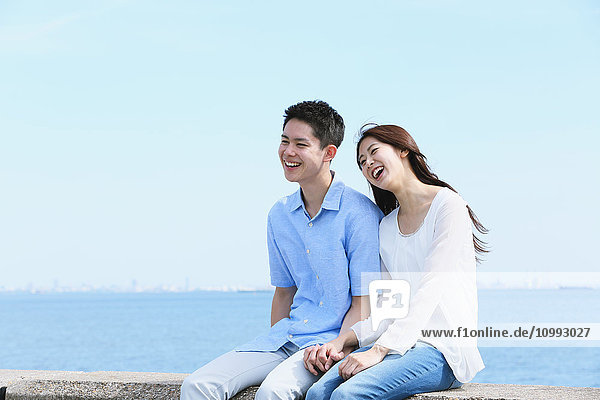 Young Japanese couple sitting on concrete wall by the sea
