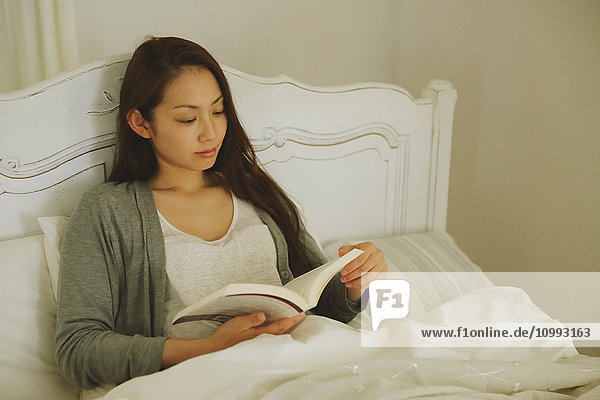 Junge attraktive japanische Frau liest im Bett