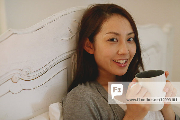 Junge attraktive japanische Frau trinkt Kaffee im Bett