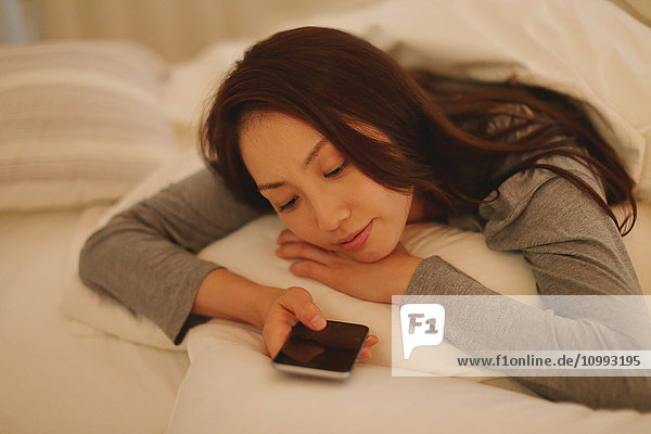 Junge attraktive japanische Frau mit Smartphone im Bett