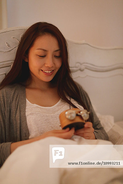 Young attractive Japanese woman setting alarm clock in bed
