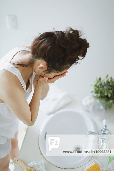 Young attractive Japanese woman washing face in the bathroom
