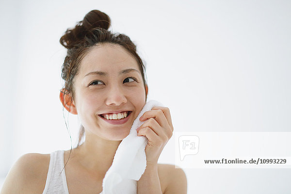 Young attractive Japanese woman wiping face with towel in the bathroom