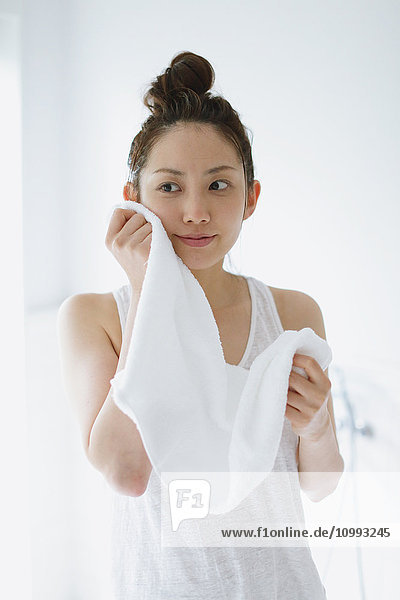 Junge attraktive japanische Frau wischt sich das Gesicht mit einem Handtuch im Badezimmer ab