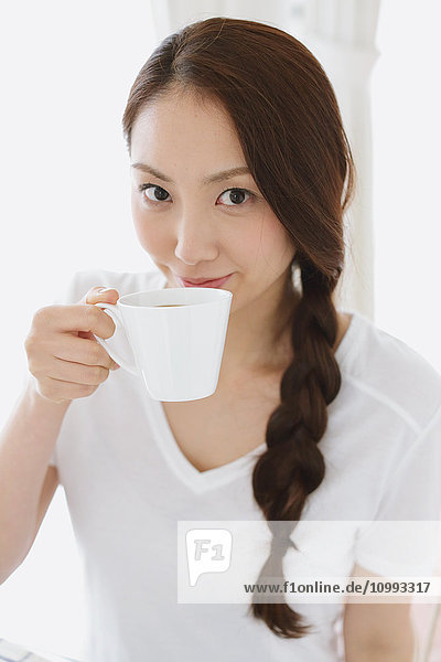 Junge attraktive japanische Frau trinkt Kaffee zu Hause
