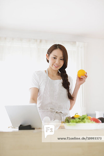 Junge attraktive Japanerin beim Kochen zu Hause mit Tablet