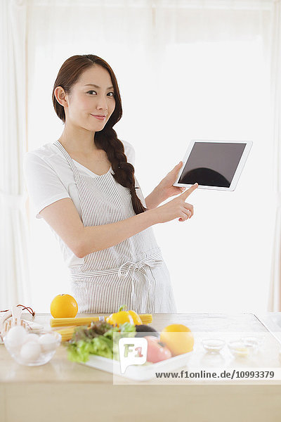 Junge attraktive Japanerin beim Kochen zu Hause mit Tablet