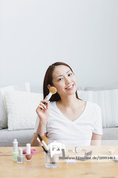 Young attractive Japanese woman doing her make-up at home