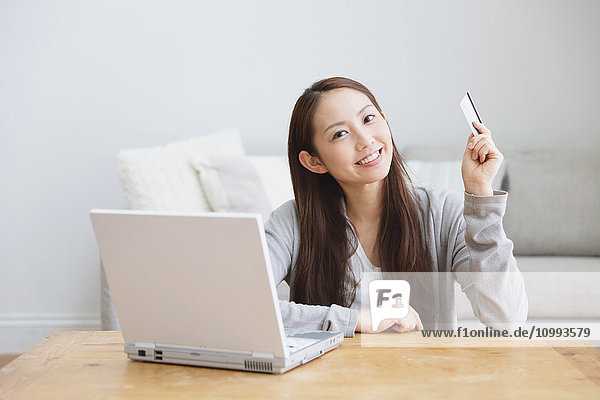 Junge attraktive japanische Frau beim Online-Shopping zu Hause