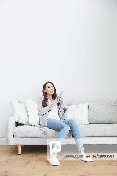 Young attractive Japanese woman with smartphone on the sofa