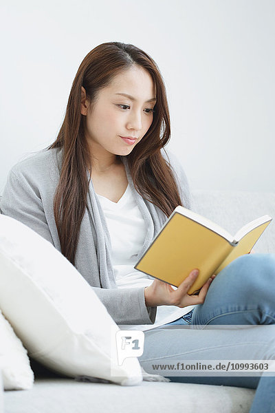 Junge attraktive Japanerin mit Buch auf dem Sofa