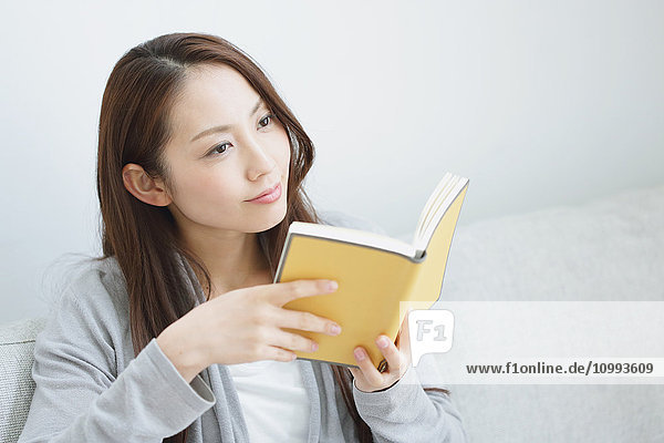 Young attractive Japanese woman with book on the sofa