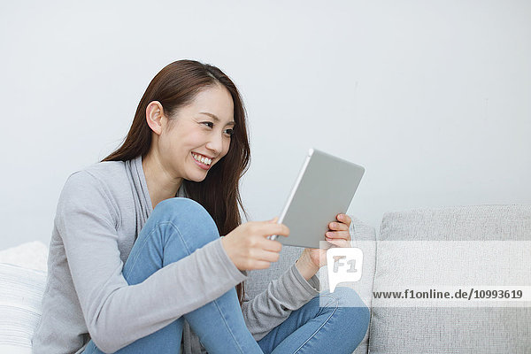 Junge attraktive Japanerin mit Tablet auf dem Sofa