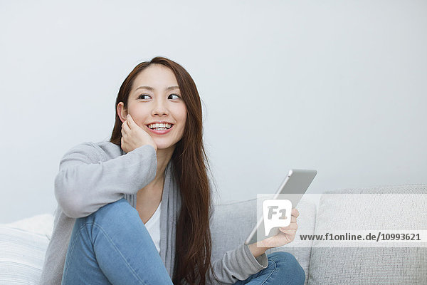 Young attractive Japanese woman with tablet on the sofa