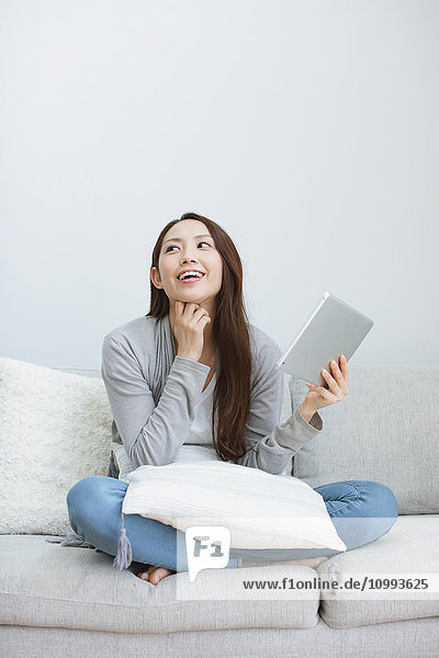 Young attractive Japanese woman with tablet on the sofa